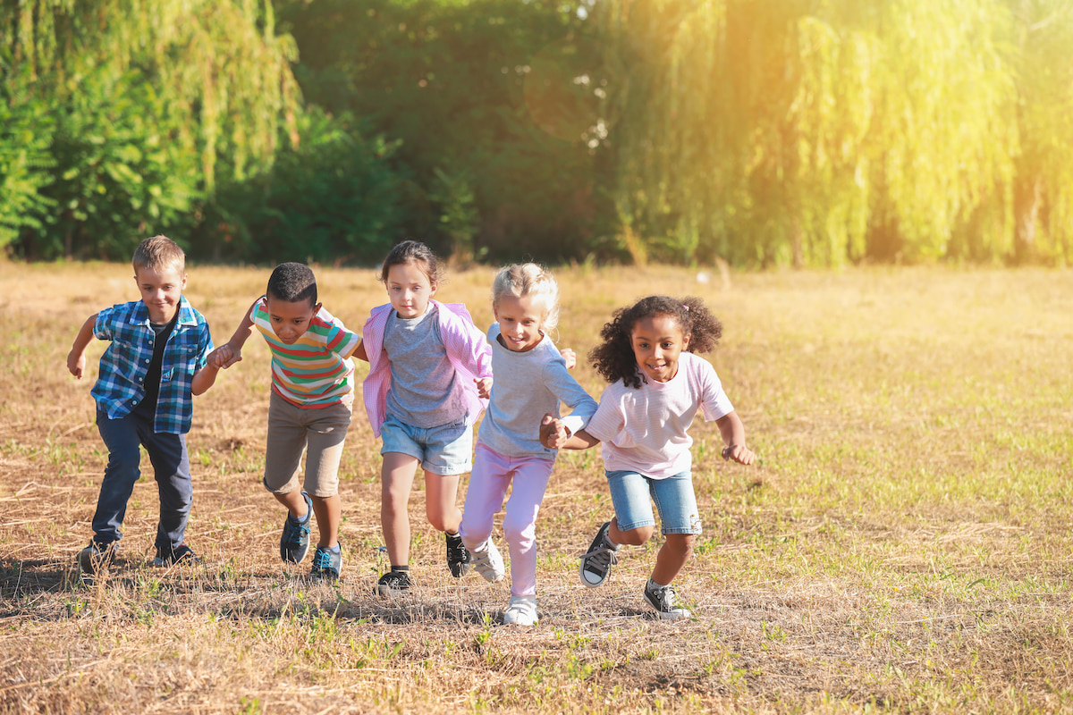A group of children running together hand-in-hand across a grassy field, smiling and laughing.